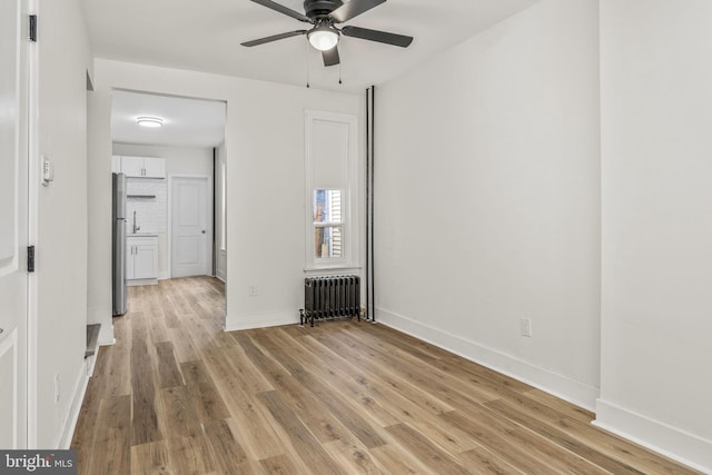 empty room featuring ceiling fan, radiator, and light hardwood / wood-style flooring