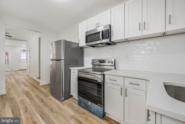 kitchen featuring sink, appliances with stainless steel finishes, decorative backsplash, white cabinets, and light wood-type flooring