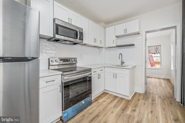 kitchen with backsplash, light wood-type flooring, stainless steel appliances, sink, and white cabinetry