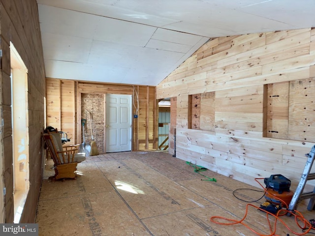 empty room with vaulted ceiling and wood walls