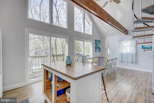 dining space with ceiling fan, beam ceiling, light wood-type flooring, and high vaulted ceiling