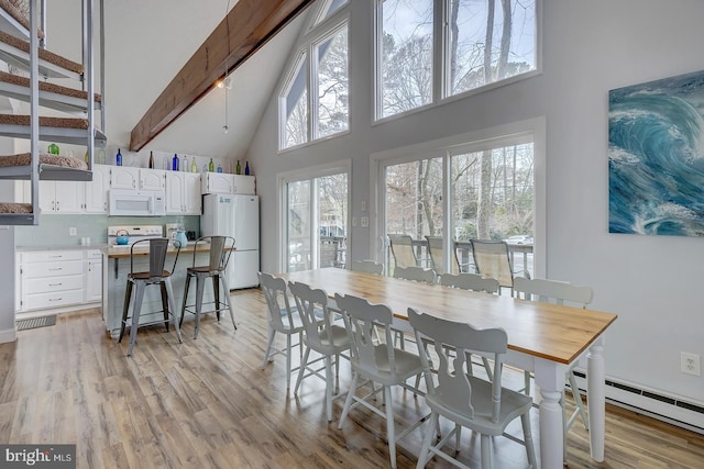 dining room featuring baseboard heating, light hardwood / wood-style flooring, a towering ceiling, and beamed ceiling