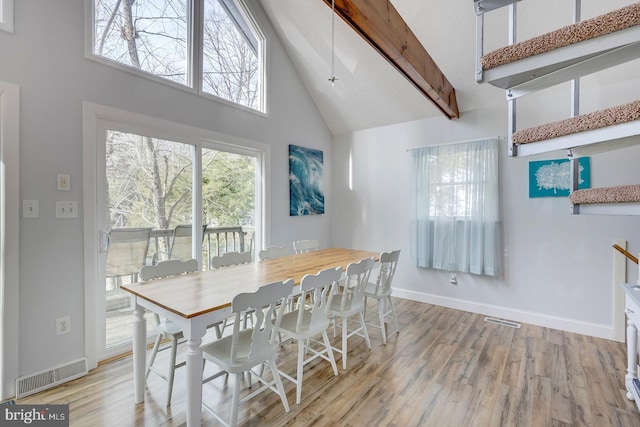 dining room featuring beam ceiling, light wood-type flooring, and high vaulted ceiling