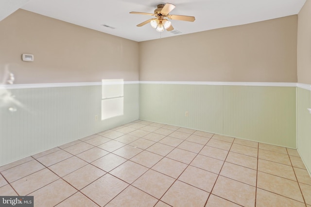 tiled empty room featuring ceiling fan and wooden walls