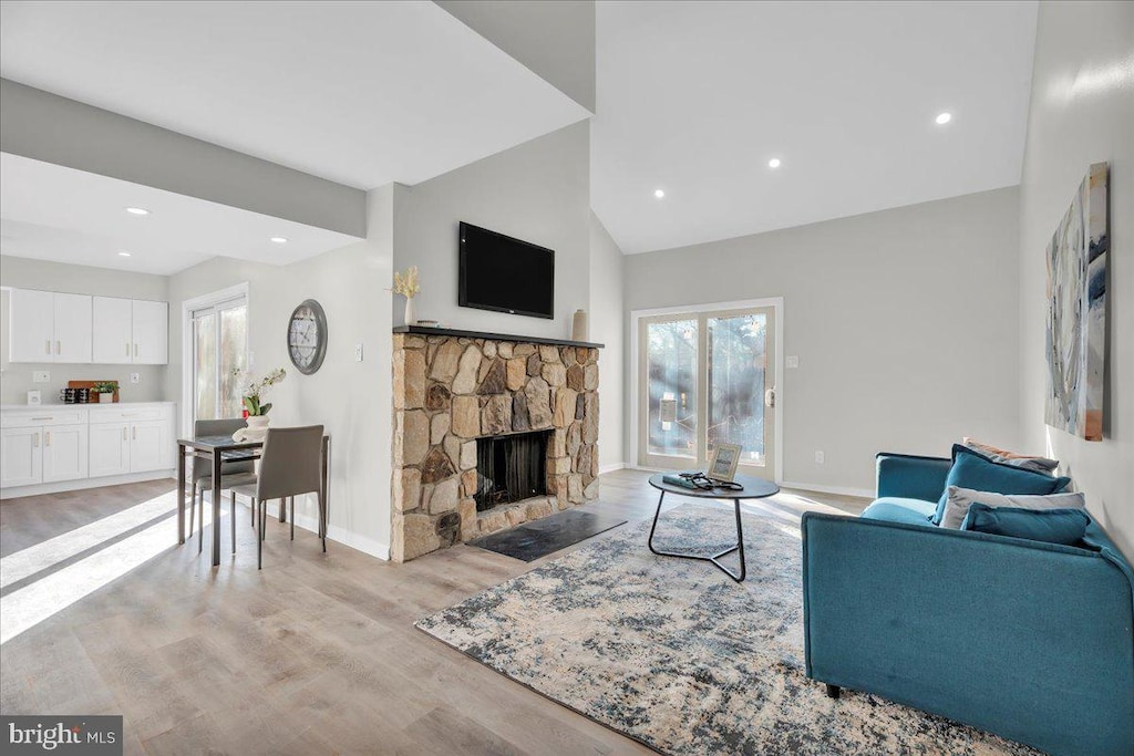 living room featuring high vaulted ceiling, light hardwood / wood-style floors, and a stone fireplace