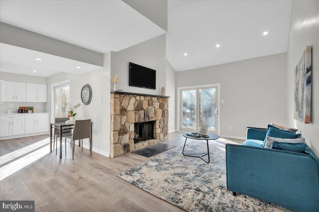 living room featuring high vaulted ceiling, light hardwood / wood-style floors, and a stone fireplace