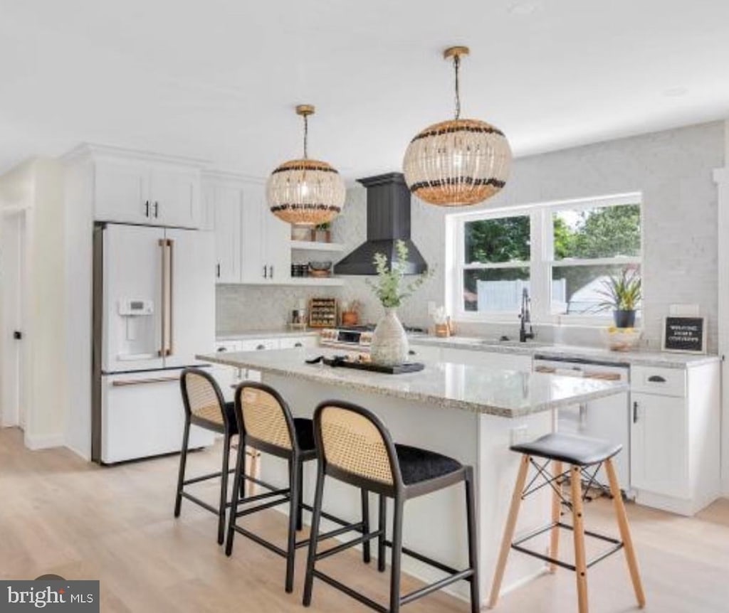 kitchen with white cabinetry, hanging light fixtures, wall chimney range hood, light hardwood / wood-style floors, and white appliances