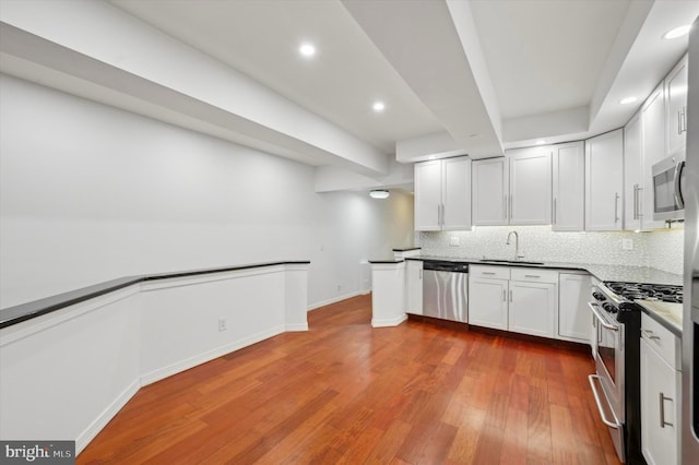 kitchen featuring hardwood / wood-style floors, decorative backsplash, sink, white cabinetry, and appliances with stainless steel finishes