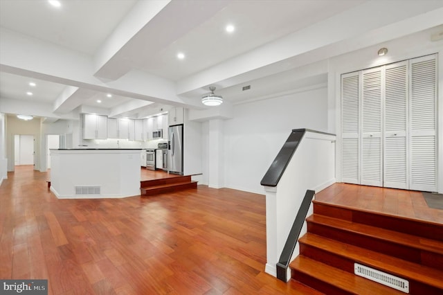 kitchen featuring kitchen peninsula, appliances with stainless steel finishes, backsplash, white cabinets, and light hardwood / wood-style flooring