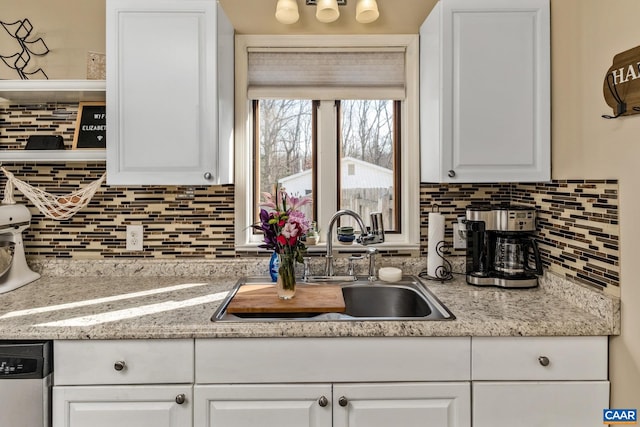 kitchen with dishwasher, light stone countertops, white cabinetry, and sink