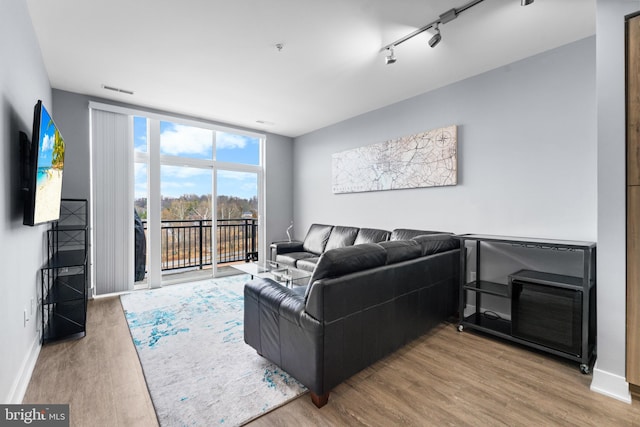 living area with baseboards, expansive windows, wood finished floors, and track lighting