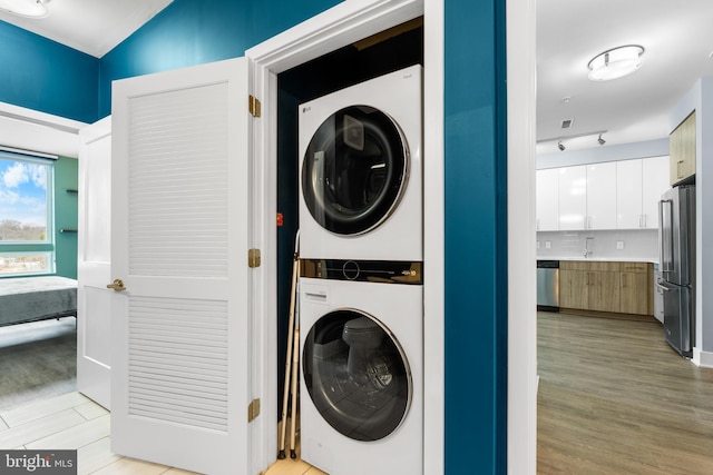 laundry area featuring laundry area, light wood-style floors, track lighting, and stacked washer / drying machine