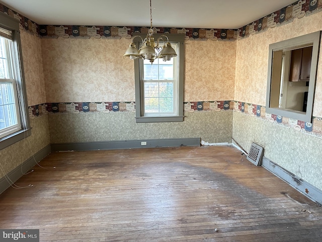 unfurnished dining area with wood-type flooring and an inviting chandelier