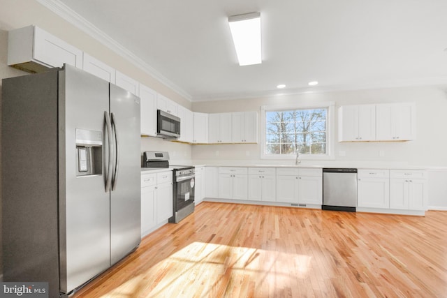 kitchen featuring light wood-type flooring, stainless steel appliances, white cabinetry, and crown molding