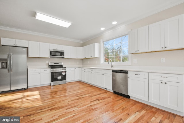 kitchen with appliances with stainless steel finishes, light wood-type flooring, white cabinetry, and crown molding