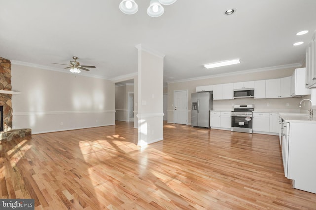 kitchen with a fireplace, white cabinets, ornamental molding, and appliances with stainless steel finishes