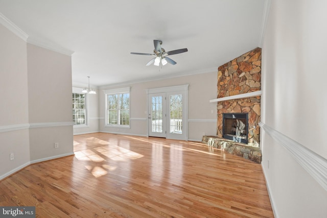 unfurnished living room with ceiling fan with notable chandelier, crown molding, light wood-type flooring, and a fireplace