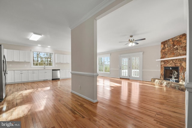 unfurnished living room with a stone fireplace, crown molding, and light wood-type flooring