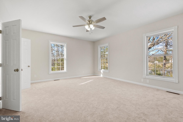 unfurnished room with ceiling fan, light colored carpet, and plenty of natural light