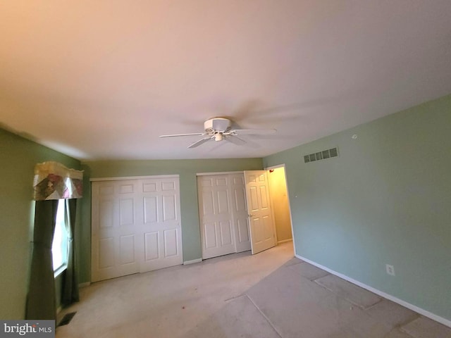 unfurnished bedroom featuring light colored carpet, a ceiling fan, baseboards, visible vents, and multiple closets