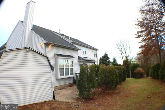 exterior space featuring a shingled roof, a chimney, and a lawn