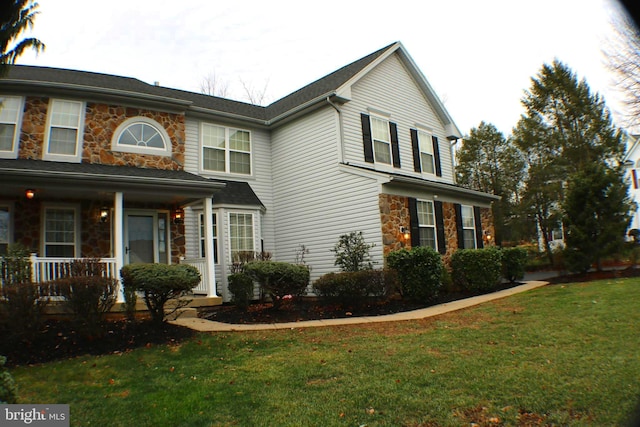 view of front of home featuring a front yard, stone siding, and covered porch