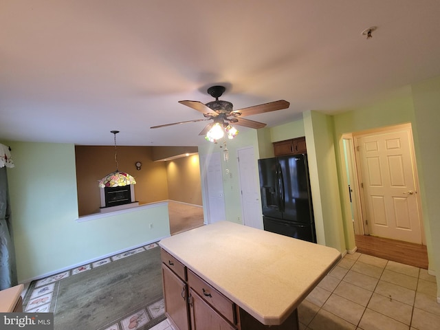 kitchen featuring light tile patterned flooring, decorative light fixtures, black refrigerator with ice dispenser, a kitchen island, and ceiling fan