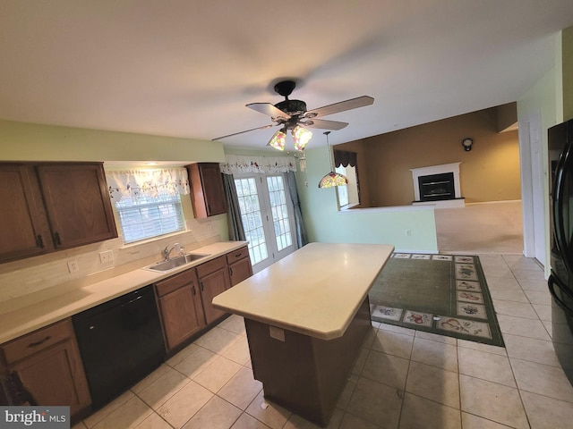 kitchen with a fireplace with raised hearth, light countertops, a kitchen island, a sink, and black appliances