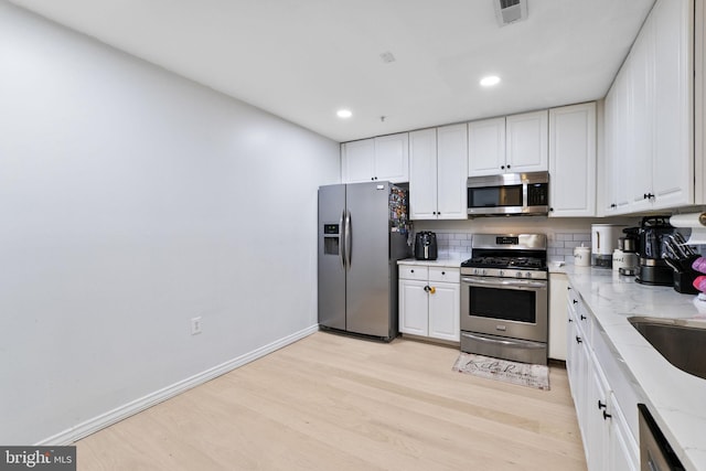 kitchen with light stone countertops, stainless steel appliances, backsplash, light hardwood / wood-style floors, and white cabinets