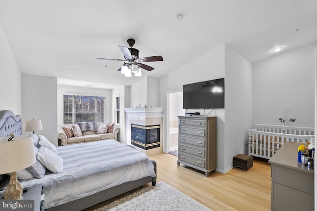 bedroom with ceiling fan, vaulted ceiling, a multi sided fireplace, and light hardwood / wood-style flooring