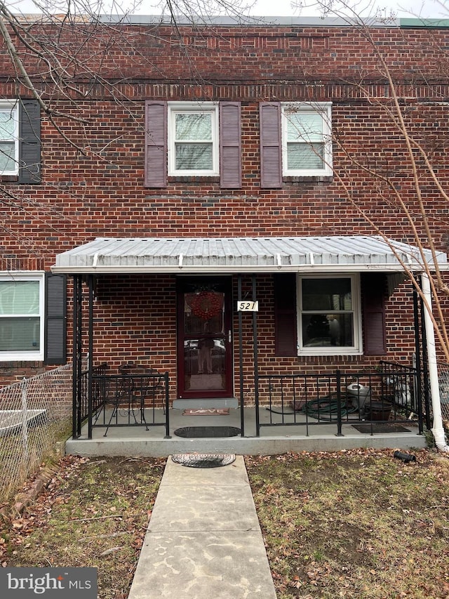 view of property featuring covered porch, fence, and brick siding