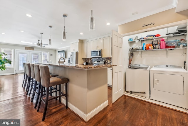 kitchen with decorative light fixtures, a breakfast bar area, appliances with stainless steel finishes, white cabinetry, and separate washer and dryer