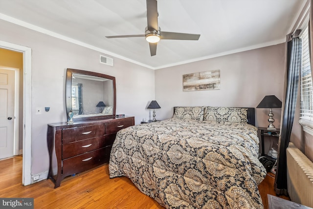 bedroom with visible vents, radiator heating unit, ceiling fan, crown molding, and light wood-style floors