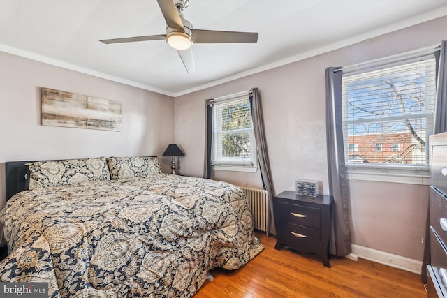 bedroom with crown molding, radiator, ceiling fan, wood finished floors, and baseboards