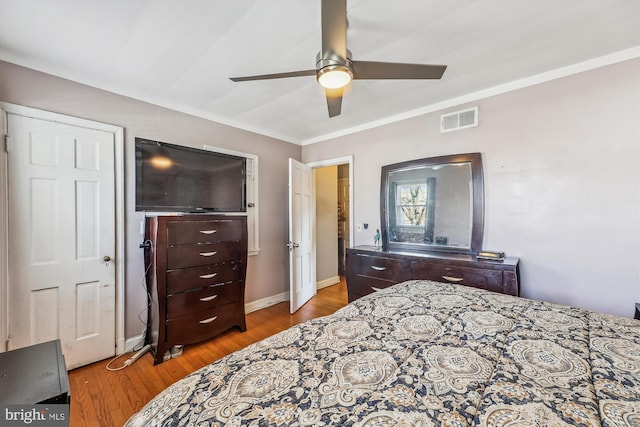 bedroom featuring wood finished floors, a ceiling fan, baseboards, visible vents, and crown molding