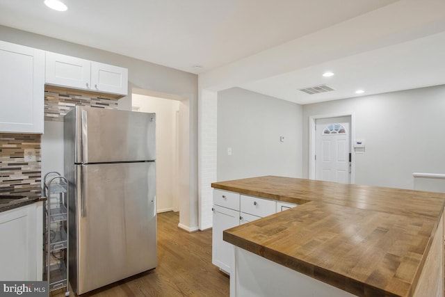 kitchen with wooden counters, white cabinets, decorative backsplash, wood-type flooring, and stainless steel refrigerator