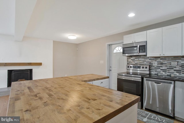 kitchen featuring decorative backsplash, appliances with stainless steel finishes, a fireplace, butcher block countertops, and white cabinetry