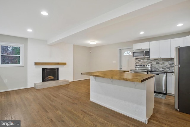 kitchen featuring butcher block counters, white cabinetry, stainless steel appliances, tasteful backsplash, and wood-type flooring