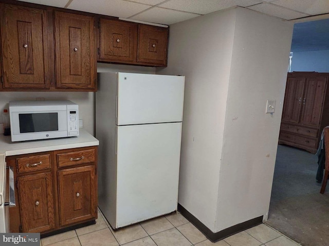 kitchen with a paneled ceiling, light tile patterned flooring, and white appliances