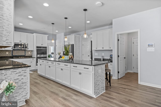 kitchen with white cabinetry, hanging light fixtures, dark stone counters, a kitchen island, and appliances with stainless steel finishes