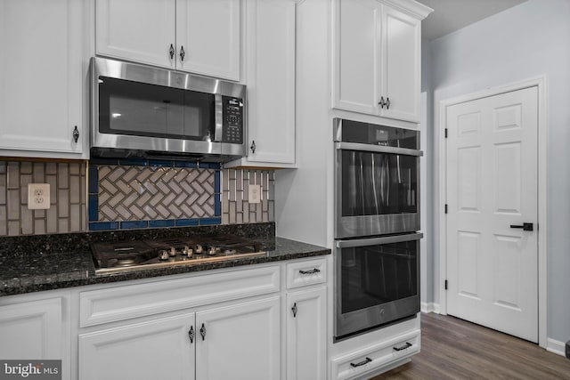 kitchen with dark wood-type flooring, stainless steel appliances, white cabinetry, and dark stone counters