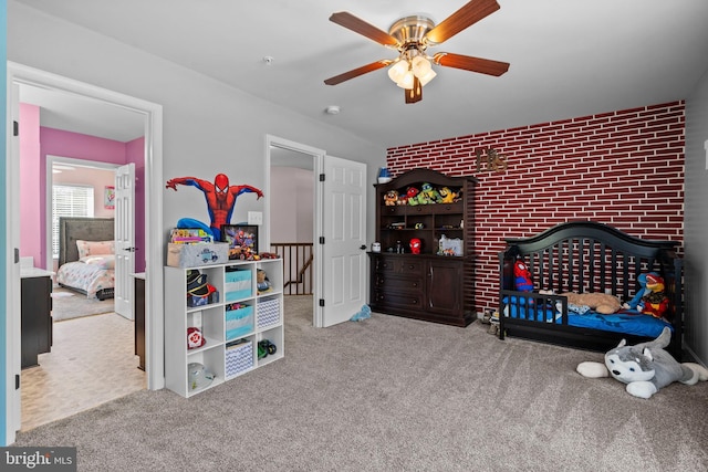 carpeted bedroom featuring a crib, ceiling fan, and brick wall