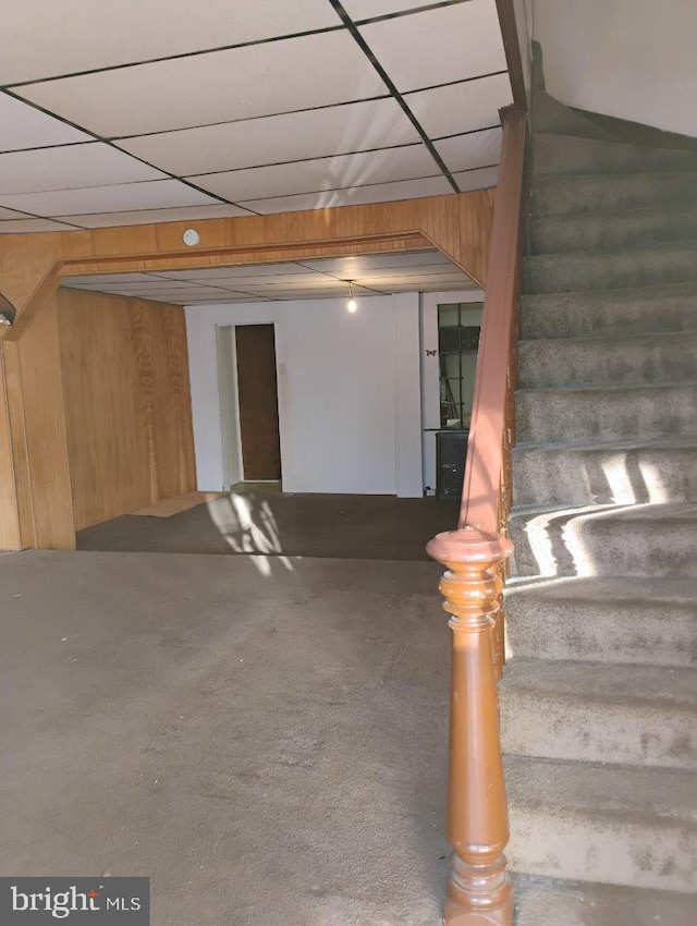 basement featuring a paneled ceiling and wood walls