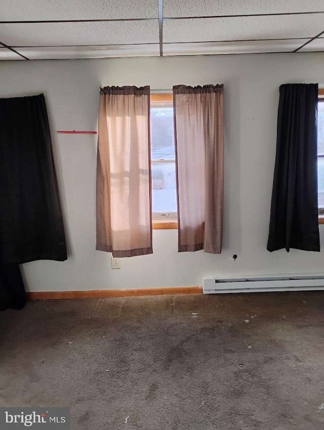 empty room with carpet flooring, a drop ceiling, and baseboard heating