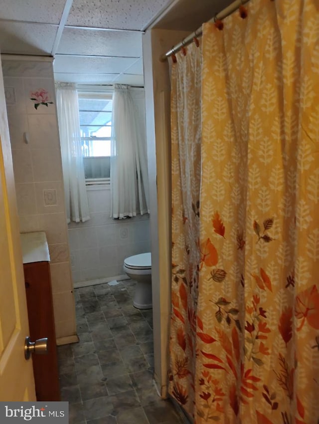 bathroom with a drop ceiling, tile walls, and toilet