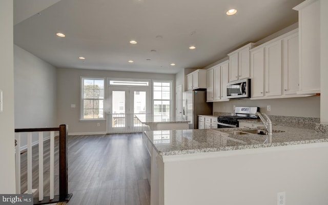 kitchen with white cabinetry, light stone countertops, sink, kitchen peninsula, and appliances with stainless steel finishes