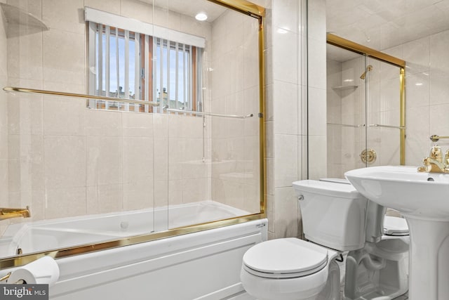 bathroom featuring combined bath / shower with glass door, toilet, and tile walls