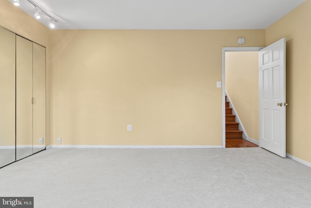 unfurnished bedroom with rail lighting, light colored carpet, and a closet