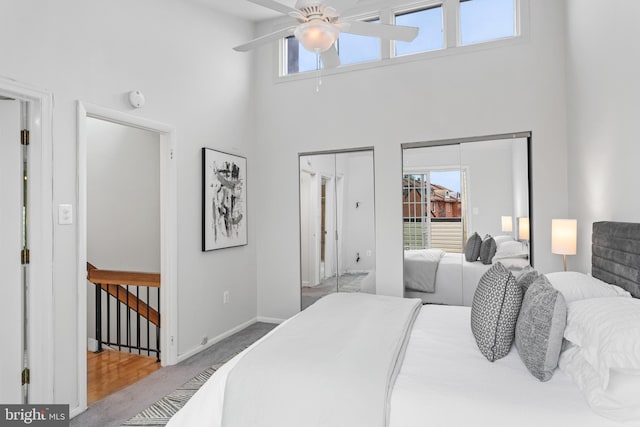 carpeted bedroom featuring multiple closets, ceiling fan, and a towering ceiling