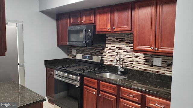 kitchen with gas stove, sink, dark stone counters, and fridge